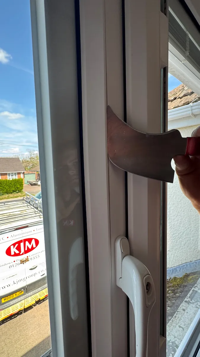 A professional window installer carefully removing the plastic bead from a window frame to extract the failed glass unit without damaging the surrounding frame.