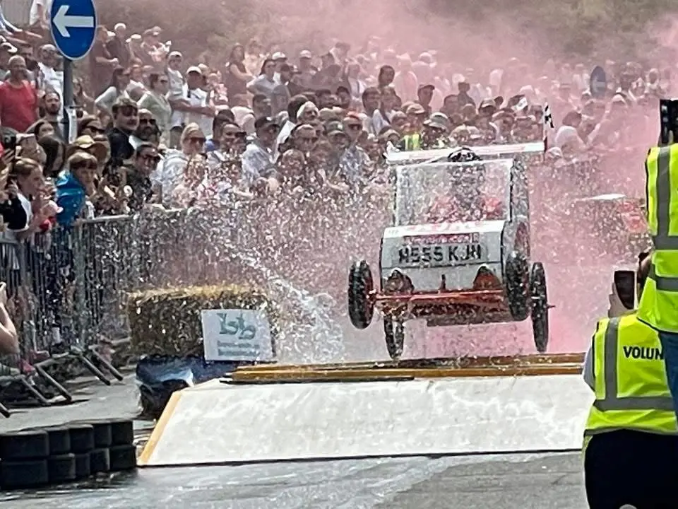 A soapbox kart going over a jump while deploying bright red smoke flares